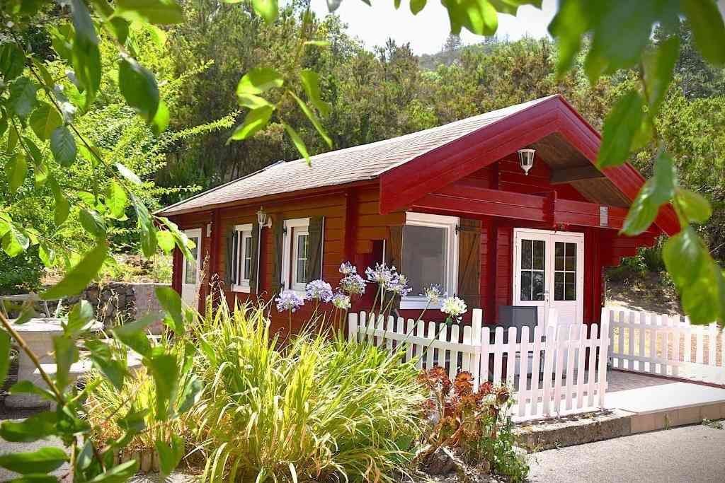 Cabaña roja con valla blanca y exuberante vegetación.