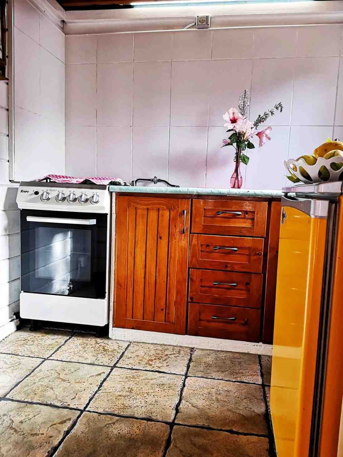 Cocina con estufa blanca, gabinetes de madera y salpicadero de azulejos; hay un jarrón con flores en la encimera.