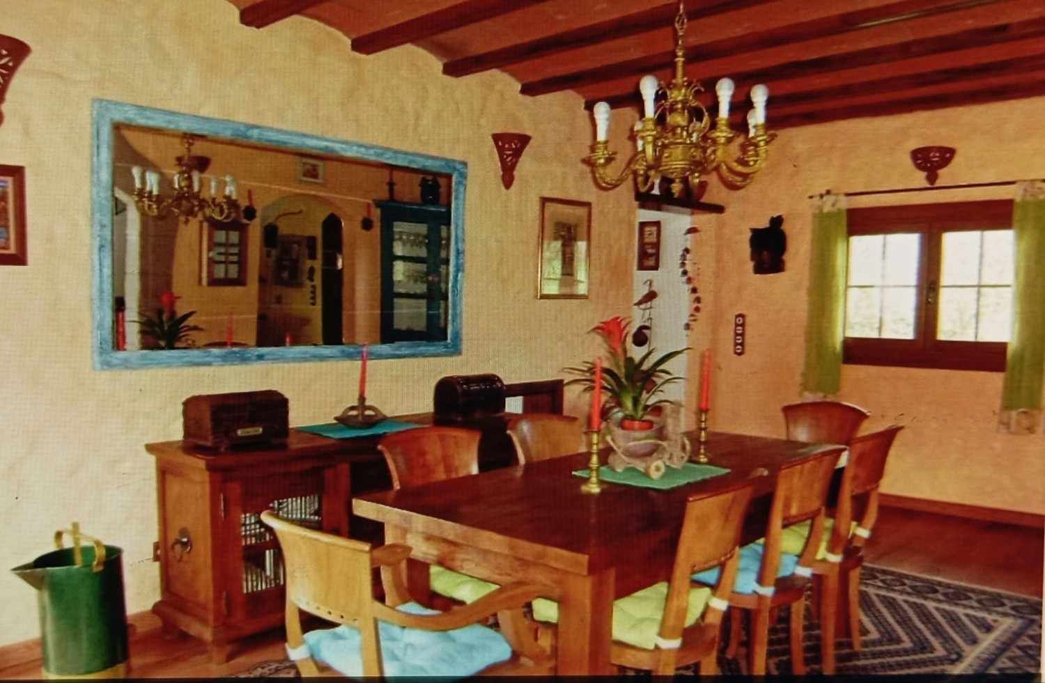 Comedor con mesa y sillas de madera, espejo, lámpara de araña y decoración rústica.
