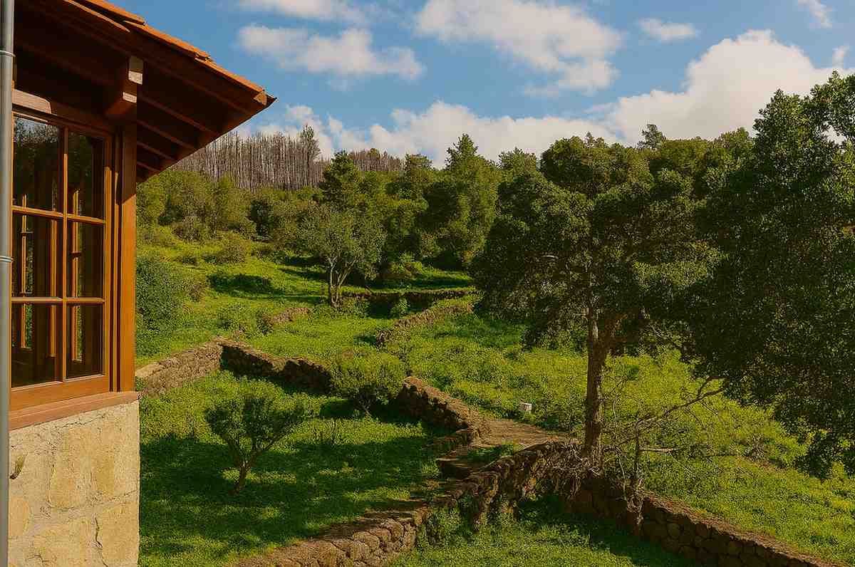 Edificio de piedra con una ventana de madera con vistas a una ladera verde con terrazas bajo un cielo azul.