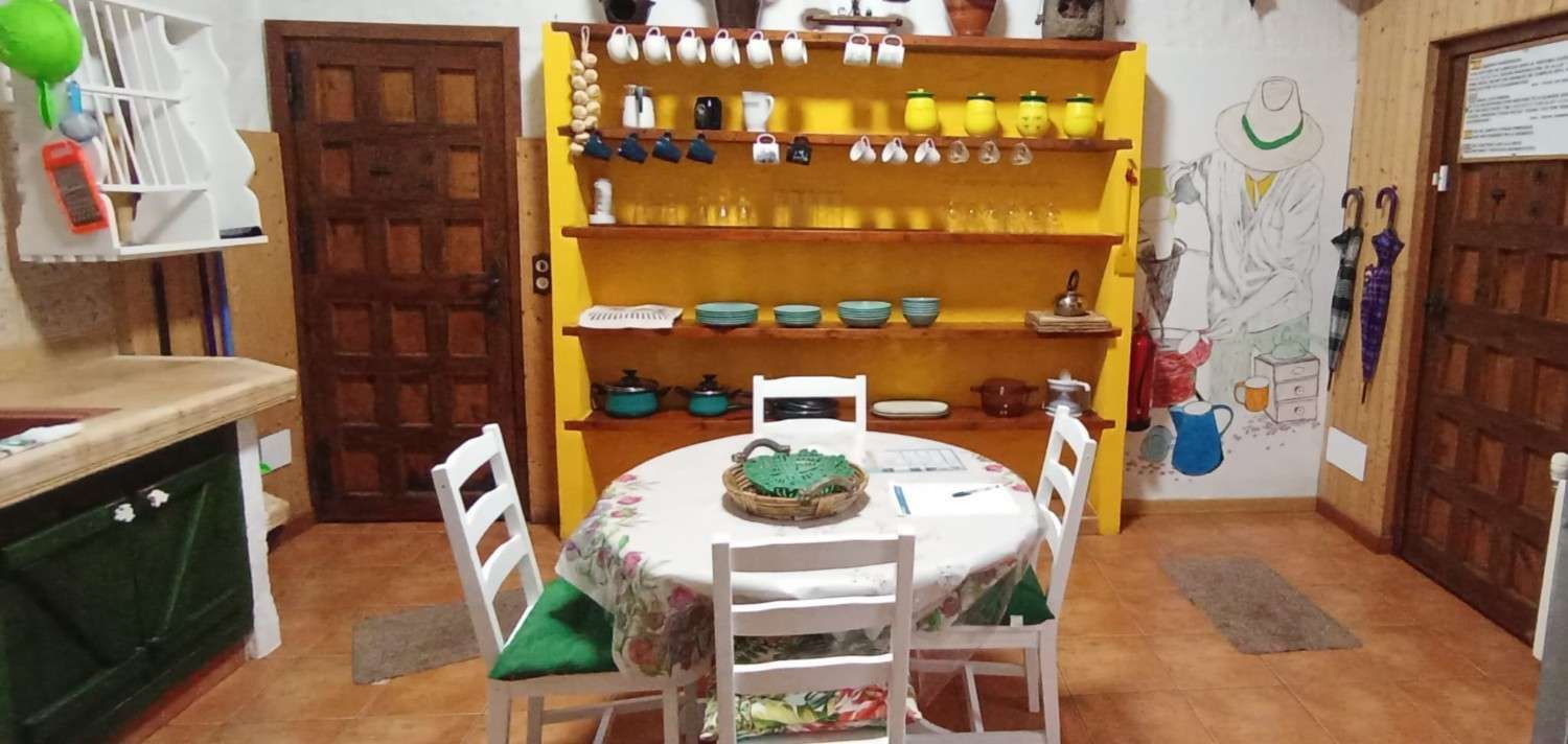 Un comedor con una mesa redonda, sillas blancas y un estante amarillo lleno de utensilios de cocina.