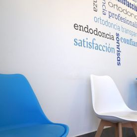 Dos sillas azules están frente a una pared blanca con palabras en español.