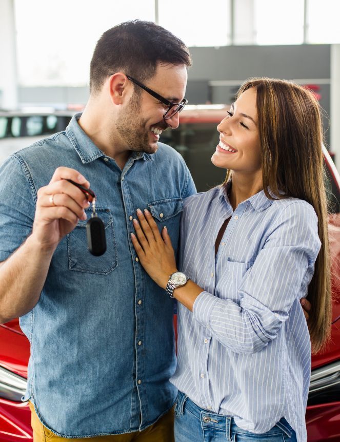 Ein Mann hält einen Autoschlüssel neben einer Frau vor einem Auto.