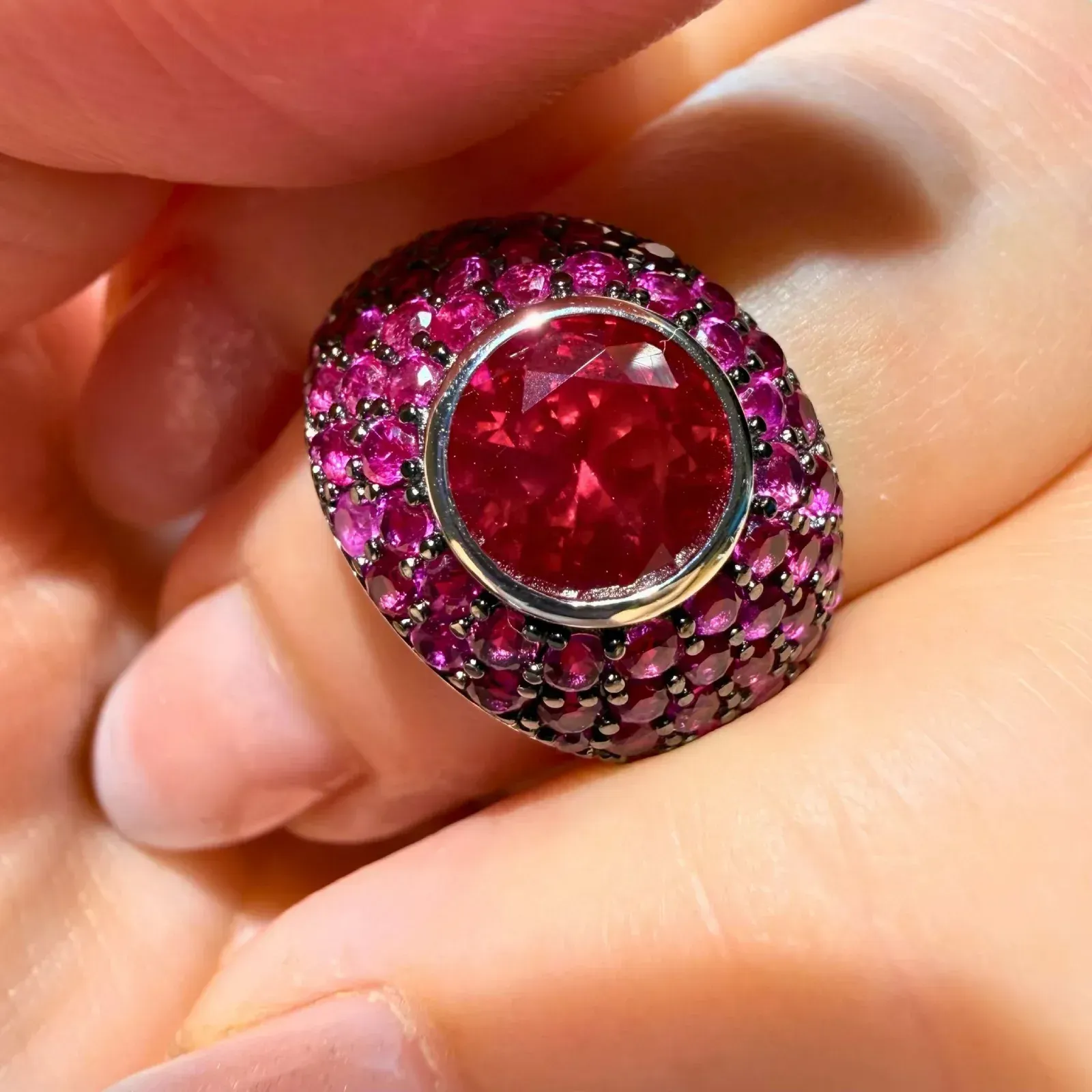 Primer plano de un anillo de plata con una gran gema roja y piedras rosas a su alrededor en una mano.