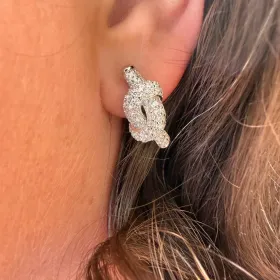 Primer plano de un brillante pendiente de aro plateado en la oreja de una persona sobre cabello castaño.
