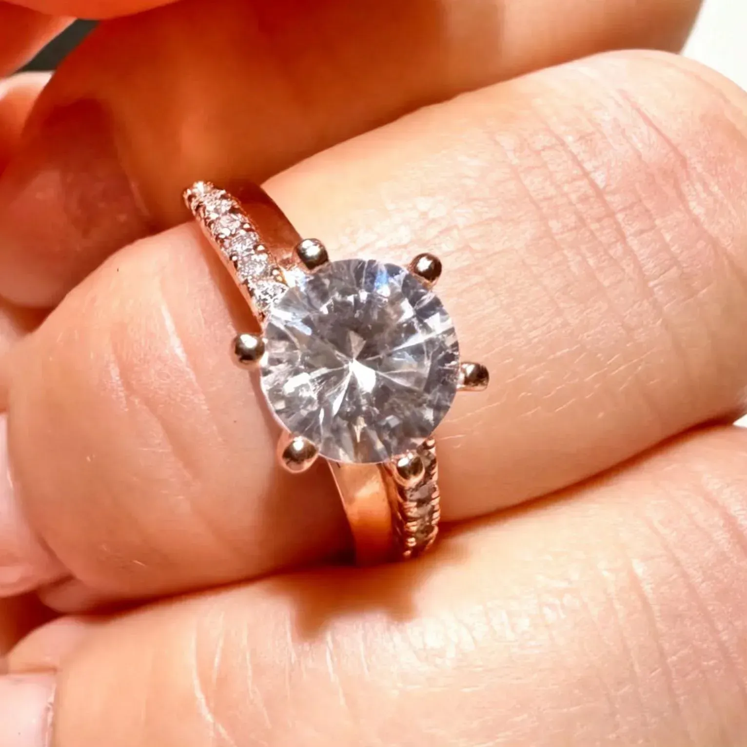 Primer plano de un anillo de plata con una gema redonda transparente en un dedo, iluminado con luz cálida.