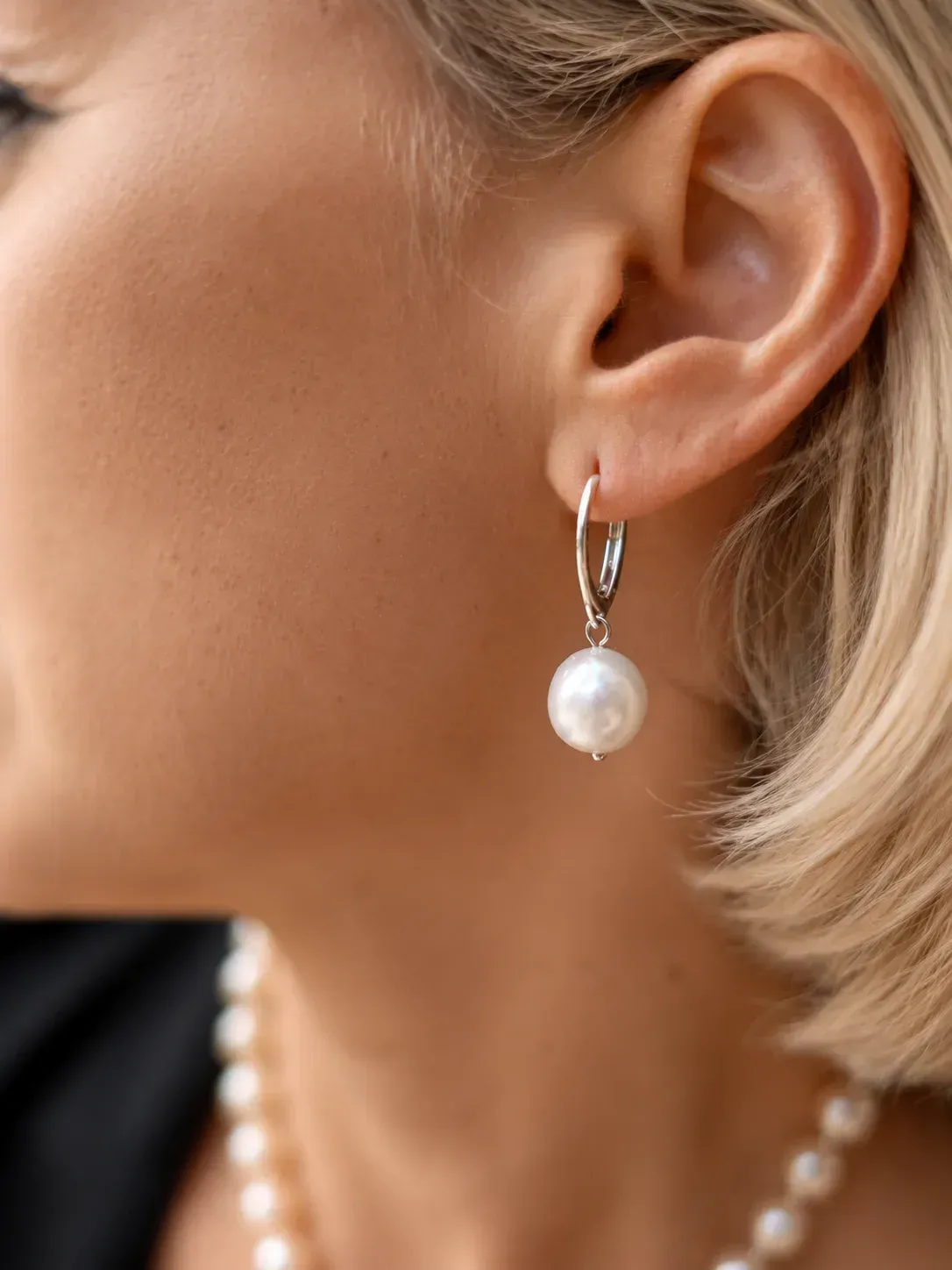 Primer plano de la oreja de una mujer que lleva un pendiente de perlas y un collar de perlas.