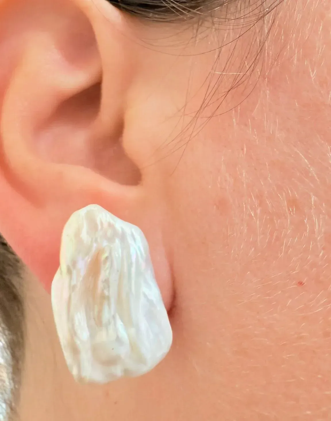 Primer plano de una oreja con un pendiente de concha blanca.