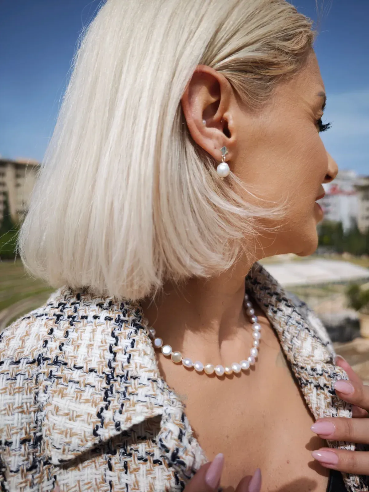 Mujer rubia con joyas de perlas y chaqueta de tweed al aire libre en un día soleado.