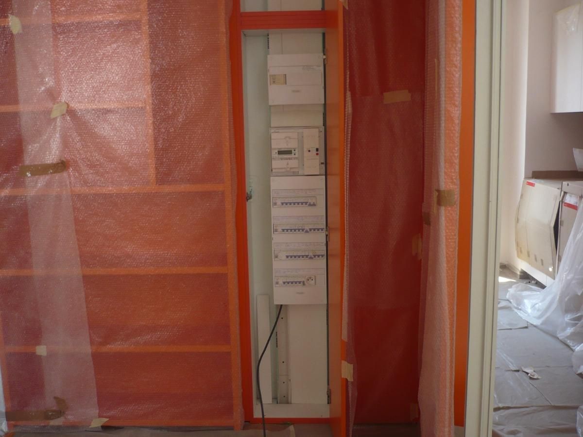 Barrière de chantier rouge autour d'une porte dans un couloir en rénovation.