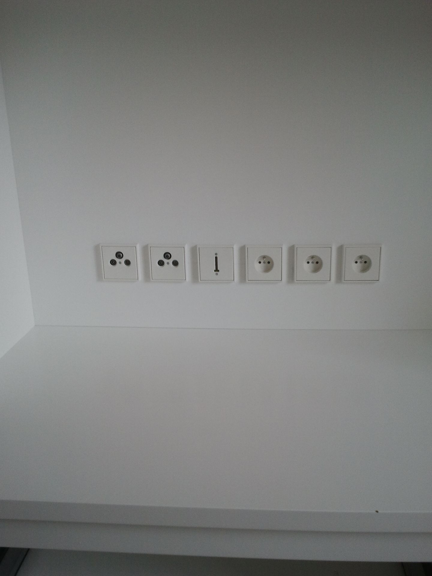 Mur avec une rangée de six prises et interrupteurs électriques blancs dans une pièce simple.