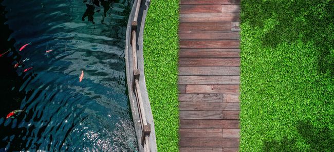 Un puente de madera sobre un cuerpo de agua al lado de un exuberante césped verde.