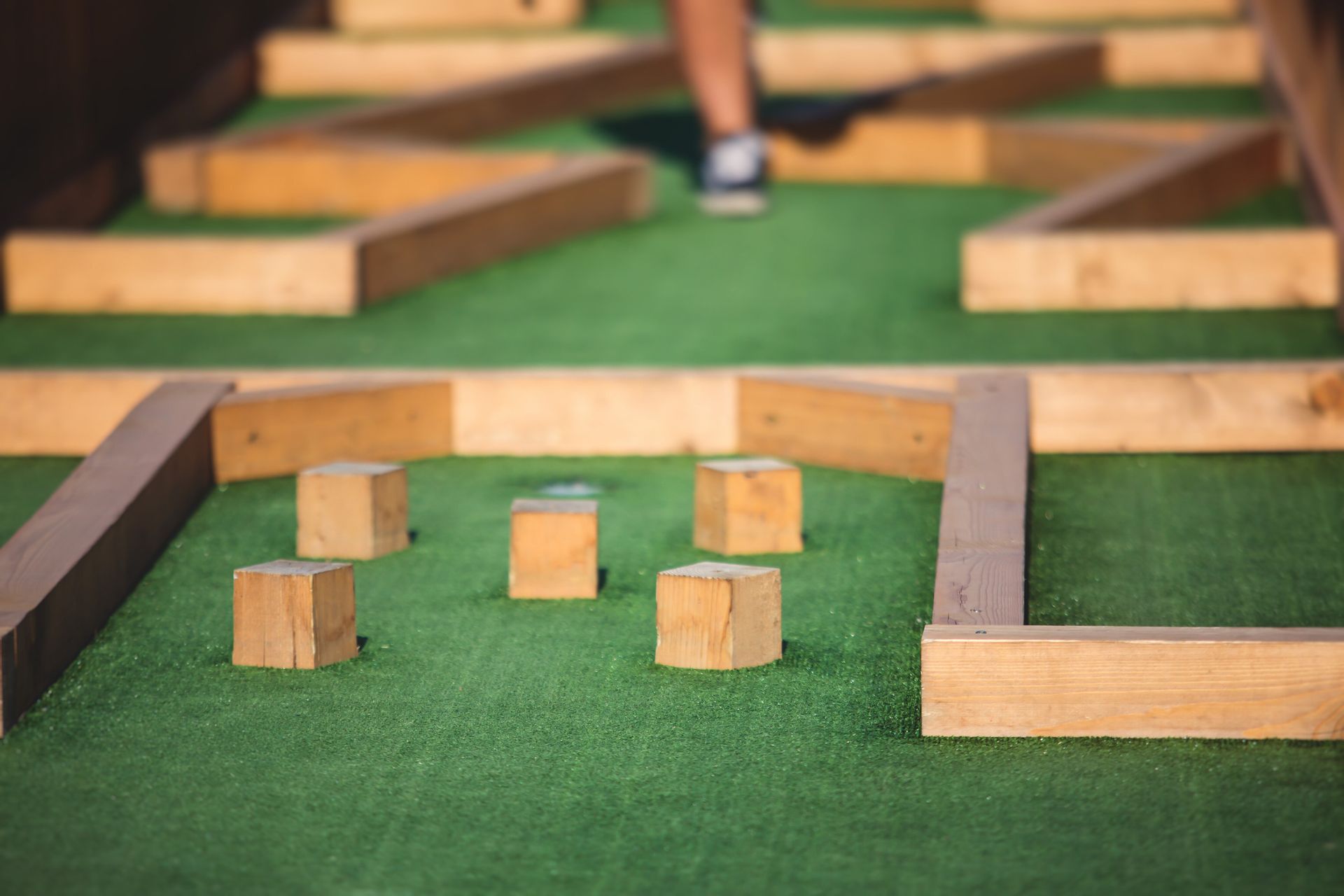 Una persona está jugando un partido de minigolf con bloques de madera en un césped verde.