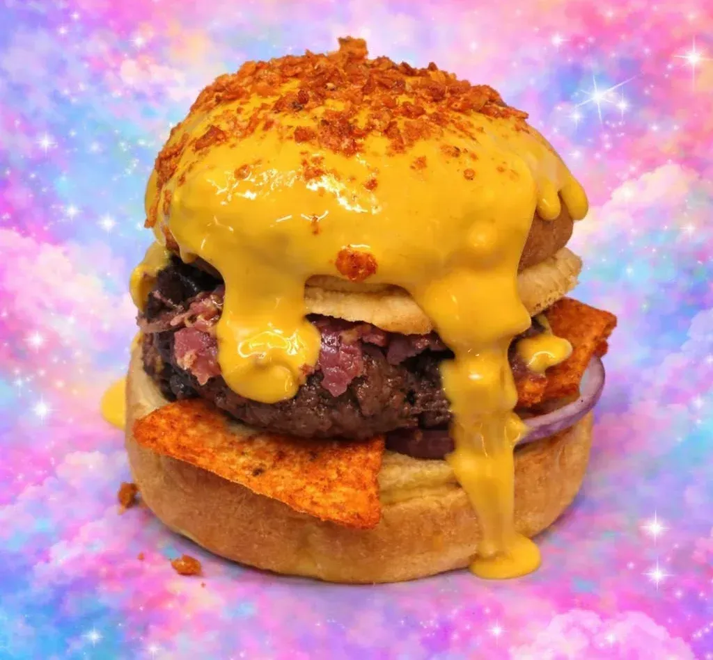 Hamburguesa con queso fundido y patatas fritas sobre un fondo pastel rosa y azul.