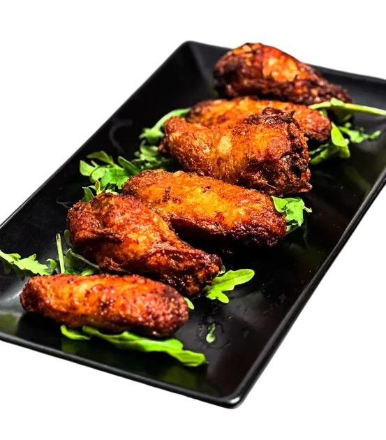 Plato negro con cuatro alitas de pollo fritas picantes adornadas con hierbas verdes.