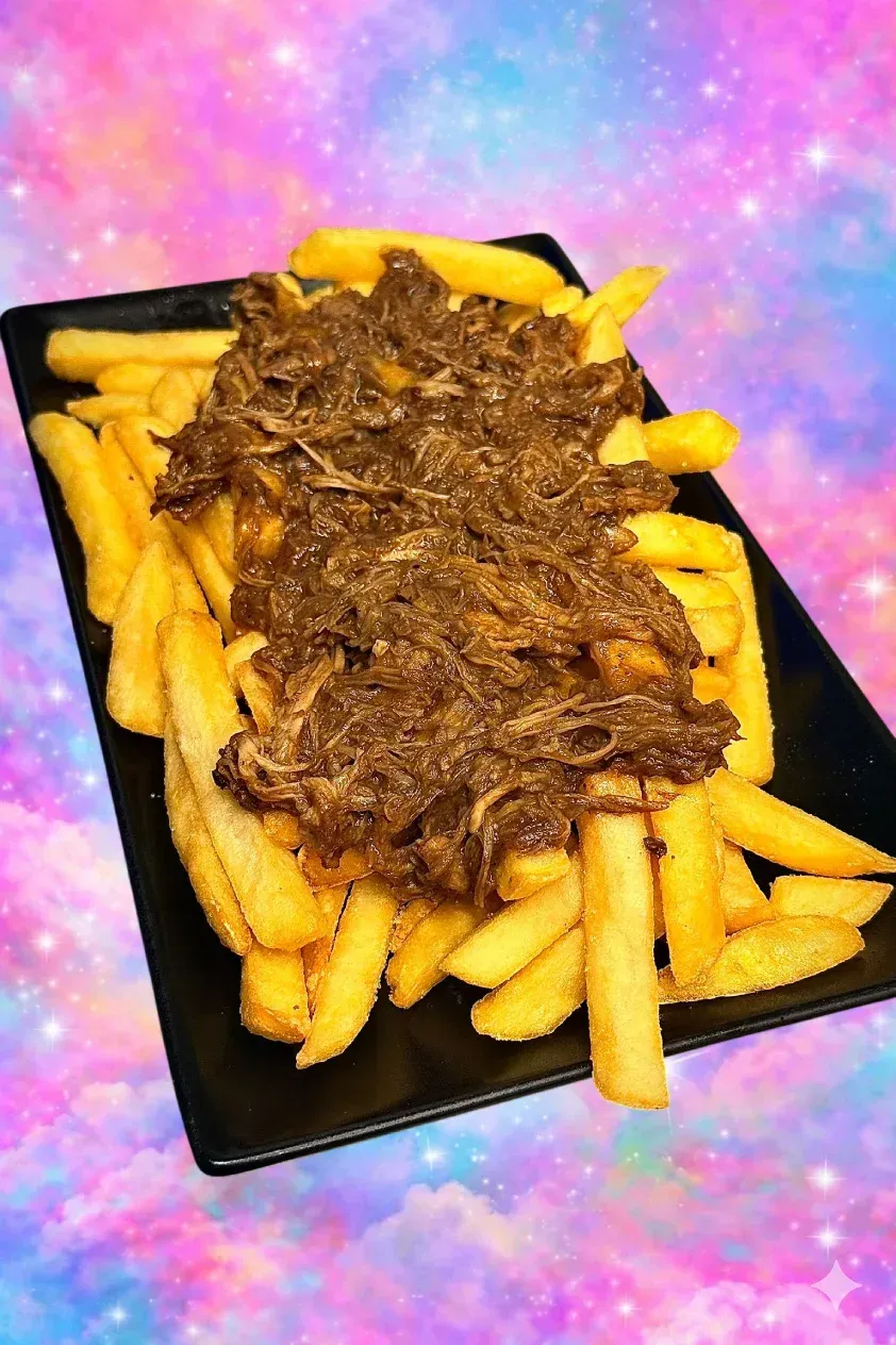 Plato negro de patatas fritas cubierto con carne desmenuzada, sobre un fondo rosa y morado.