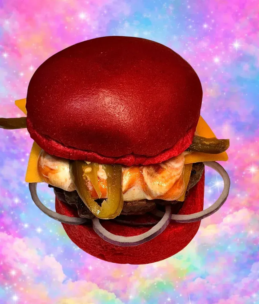 Hamburguesa roja sobre un fondo de galaxia en tonos pastel, con queso, cebolla y pepinillos.