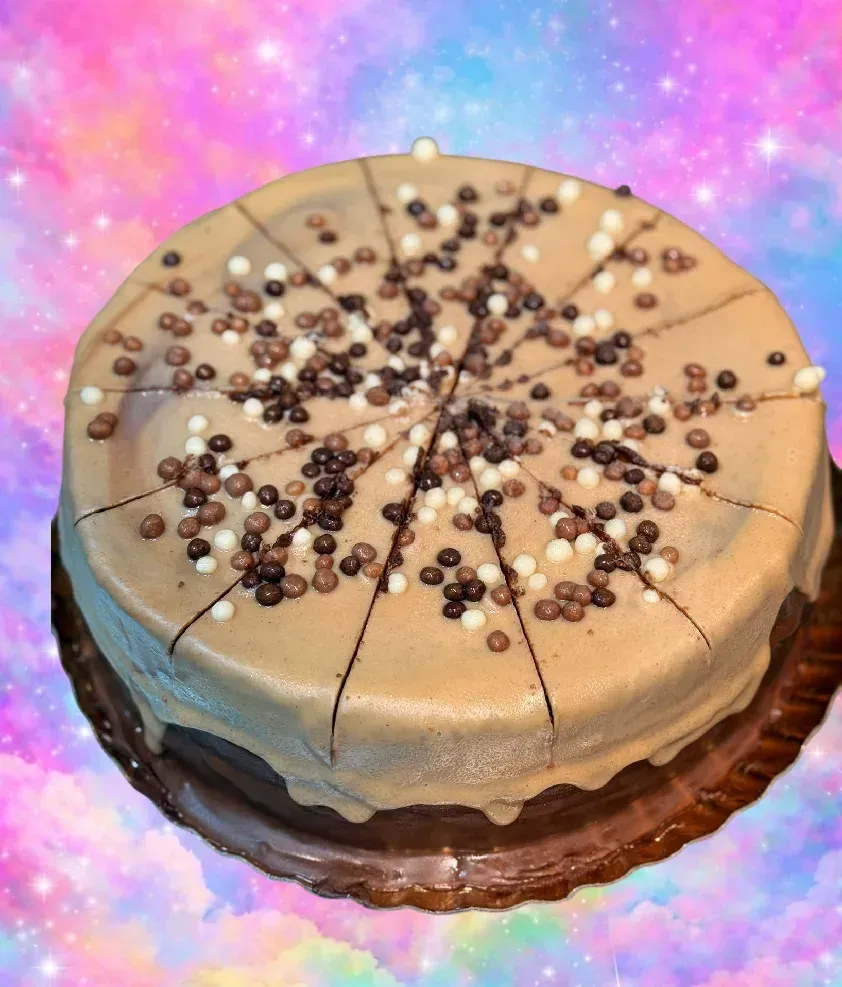 Pastel de chocolate glaseado con chispas de chocolate sobre un fondo colorido rosa y azul.