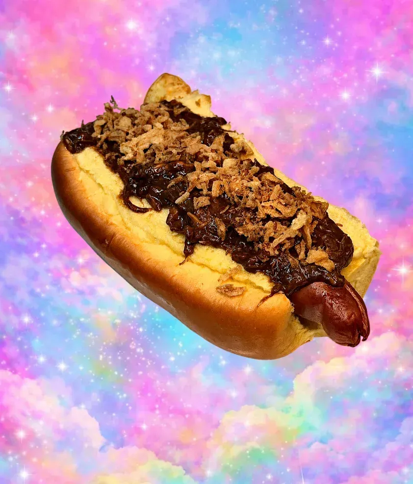 Perrito caliente cubierto con cebolla sobre un fondo de arcoíris pastel.