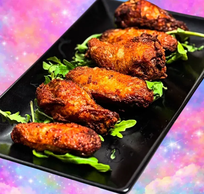 Bandeja de alitas de pollo fritas crujientes adornadas con verduras en un plato negro.