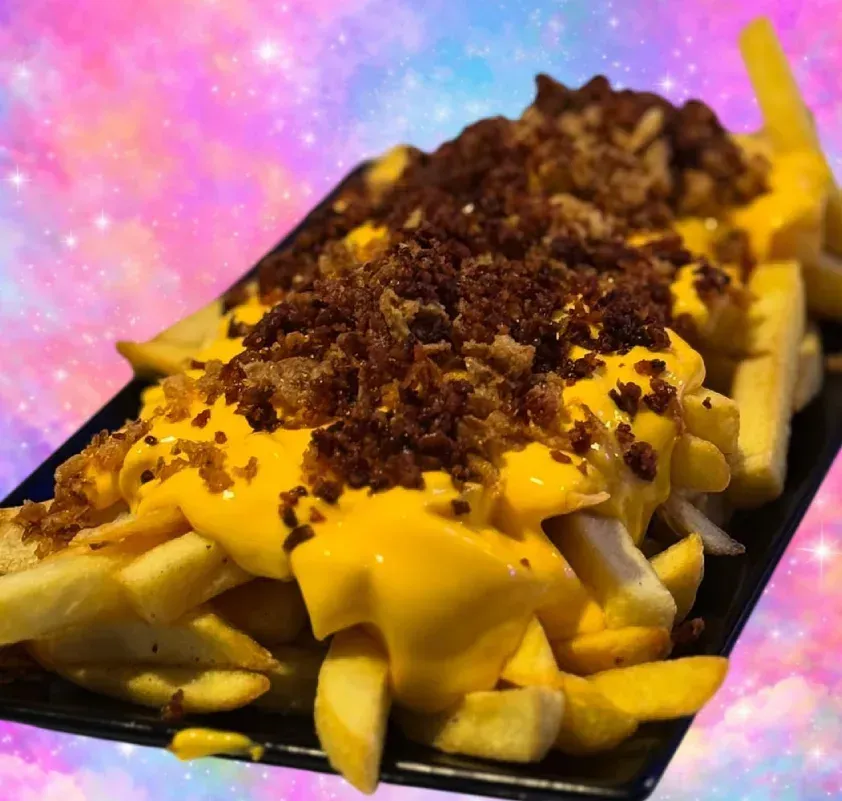 Papas fritas con queso y trocitos de tocino sobre una bandeja negra con fondo rosa-morado.
