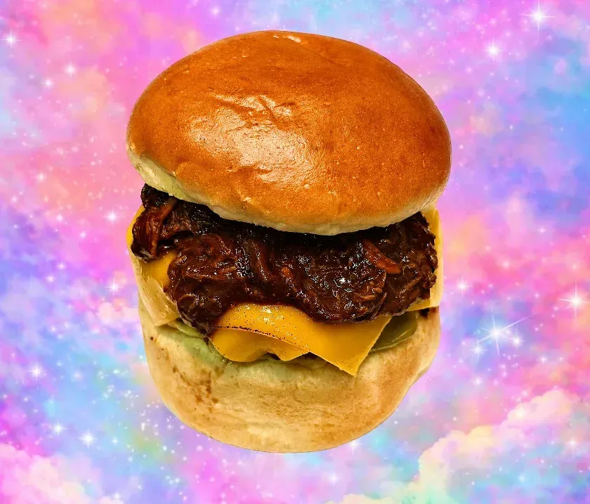 Hamburguesa con queso, pan brillante y queso derretido sobre un fondo de galaxia rosa y morado.