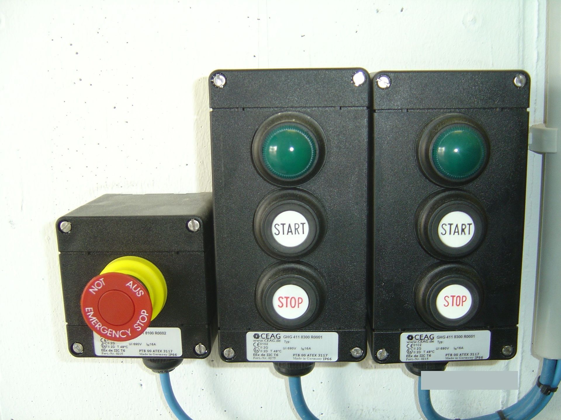 Bedienfeld mit grünen Startknöpfen, rotem Not-Aus-Knopf und schwarzen Gehäusen.