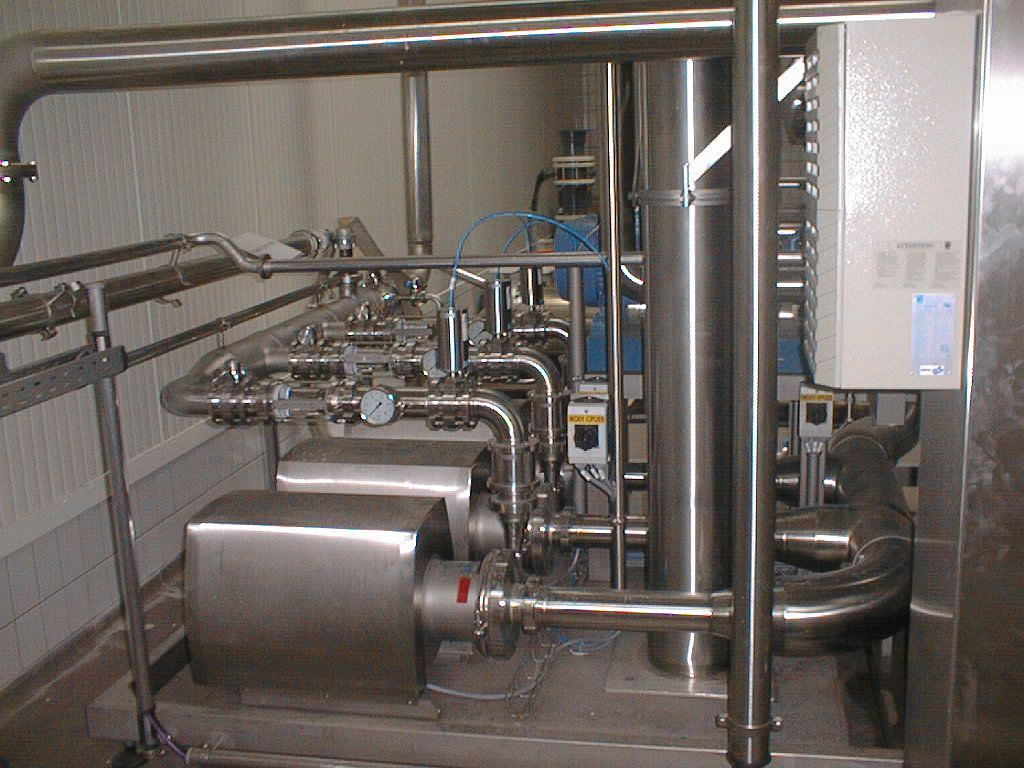 Industriemaschinen aus Edelstahl mit Rohren, Messgeräten und einem Bedienfeld in einem geschlossenen Raum.