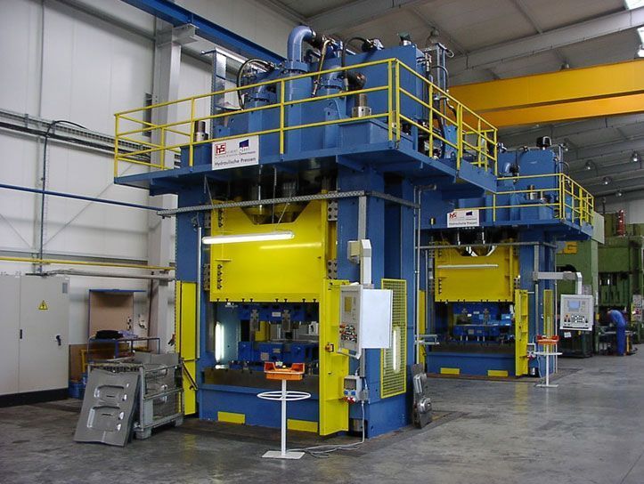 Zwei große blaue und gelbe Industriepressen in einer Fabrikumgebung.