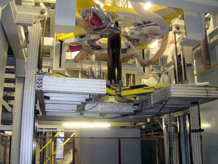 Automatisierte Industriemaschine, wahrscheinlich zum Stapeln oder Verpacken von weißen Platten in einer Fabrikumgebung.