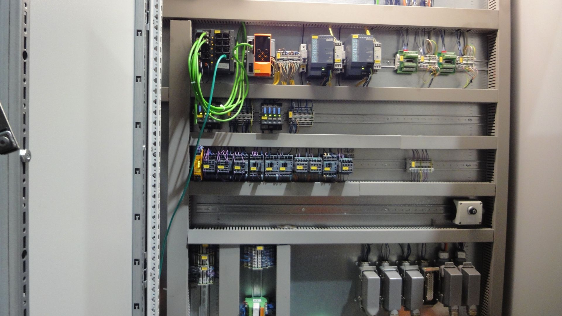 Elektrischer Schaltschrank mit auf Metallschienen montierten Drähten, Relais und Bauteilen.