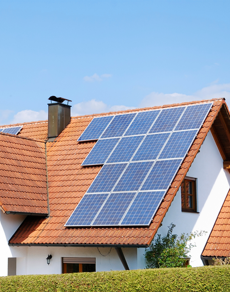 Panneaux solaires sur un toit résidentiel contre un ciel bleu ; la maison est blanche avec un toit de tuiles rouges.