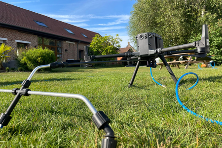 Détecteur de métaux sur trépied dans une cour herbeuse, avec tuyau bleu .
