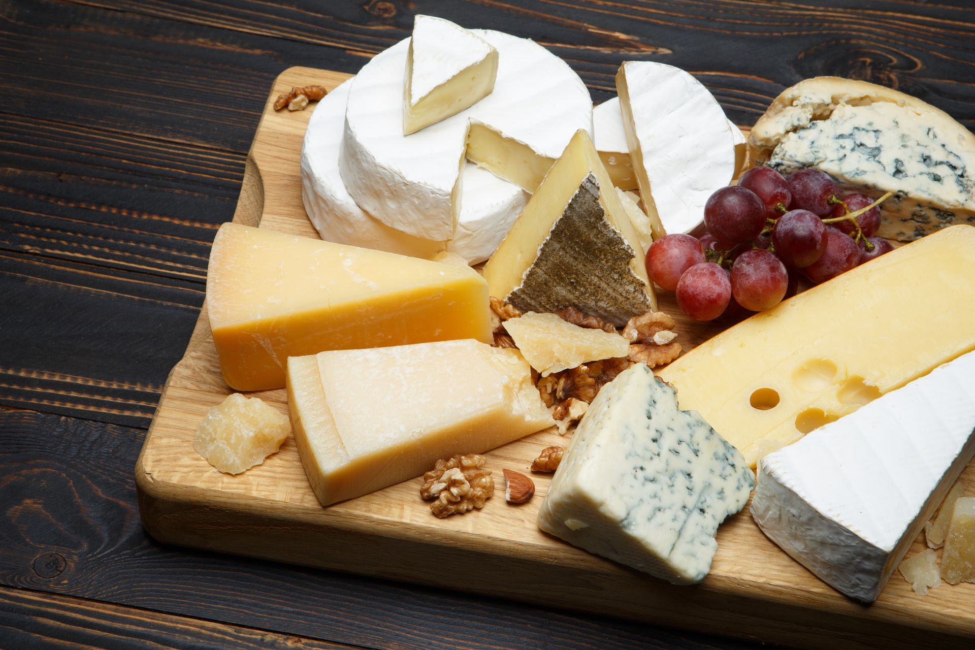 Une sélection de fromages avec des raisins disposés sur une planche en bois.