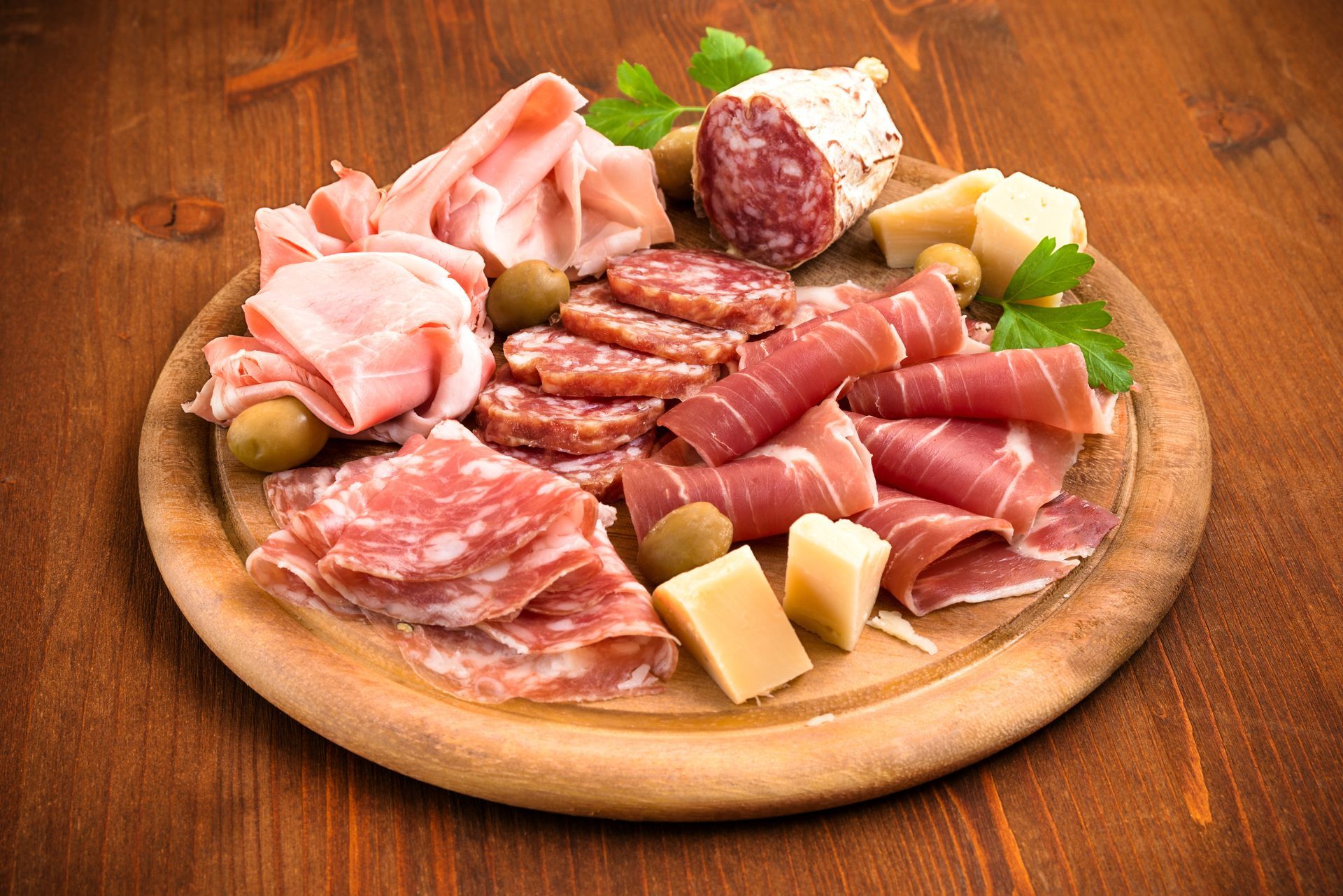 Une assiette en bois remplie de tranches de charcuteries et de fromages.