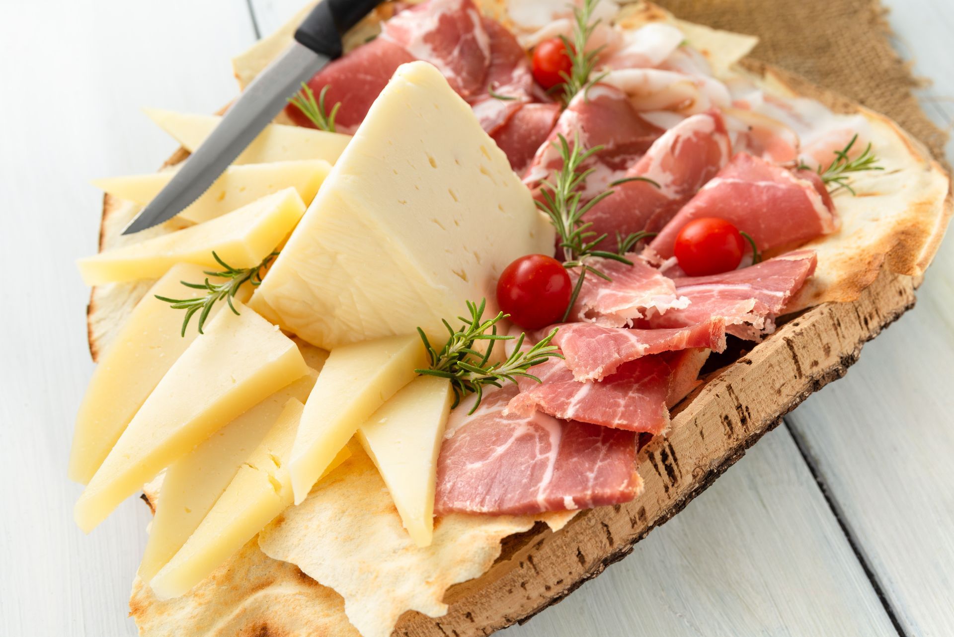 Une planche en bois avec du fromage, de la charcuterie et des tomates cerises.