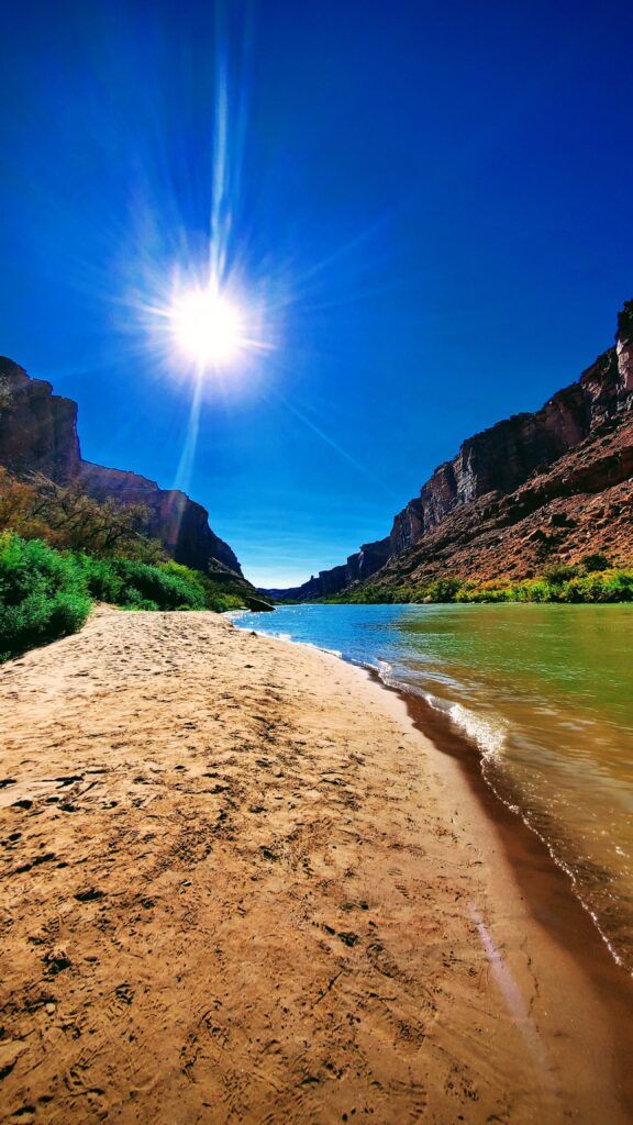 Sunny sandy beach between rocky cliffs beside green water under a bright blue sky