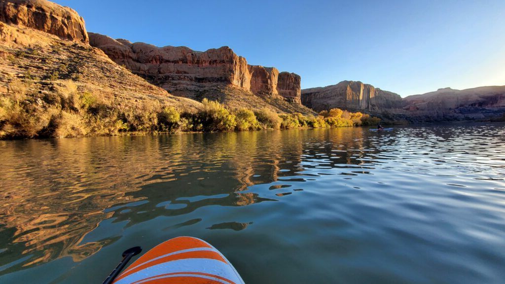 Kayak gliding on a calm river between sunlit canyon cliffs at golden hour