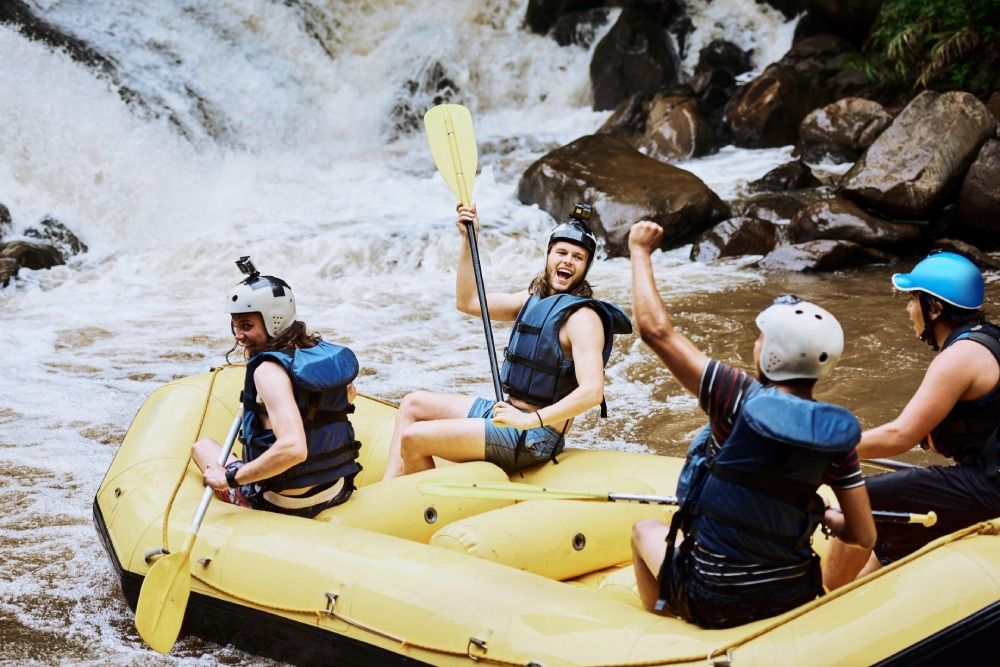 People rafting in a yellow inflatable raft through whitewater rapids near rocks