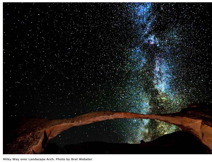 Starry night sky over an arched rock formation, with the Milky Way glowing above.