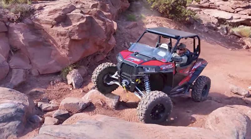 Red off-road UTV climbing rocky desert terrain among large sandstone boulders