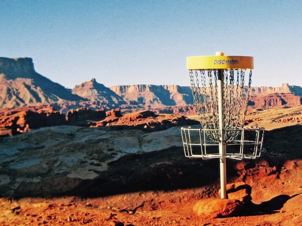 Disc golf basket on red rock desert overlook with layered canyon cliffs in the background