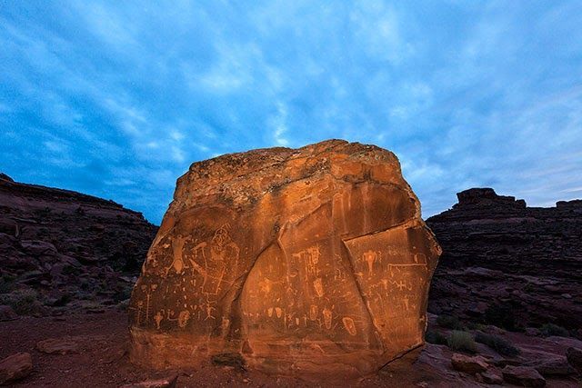 Large sunlit sandstone boulder in a desert landscape under a blue cloudy sky