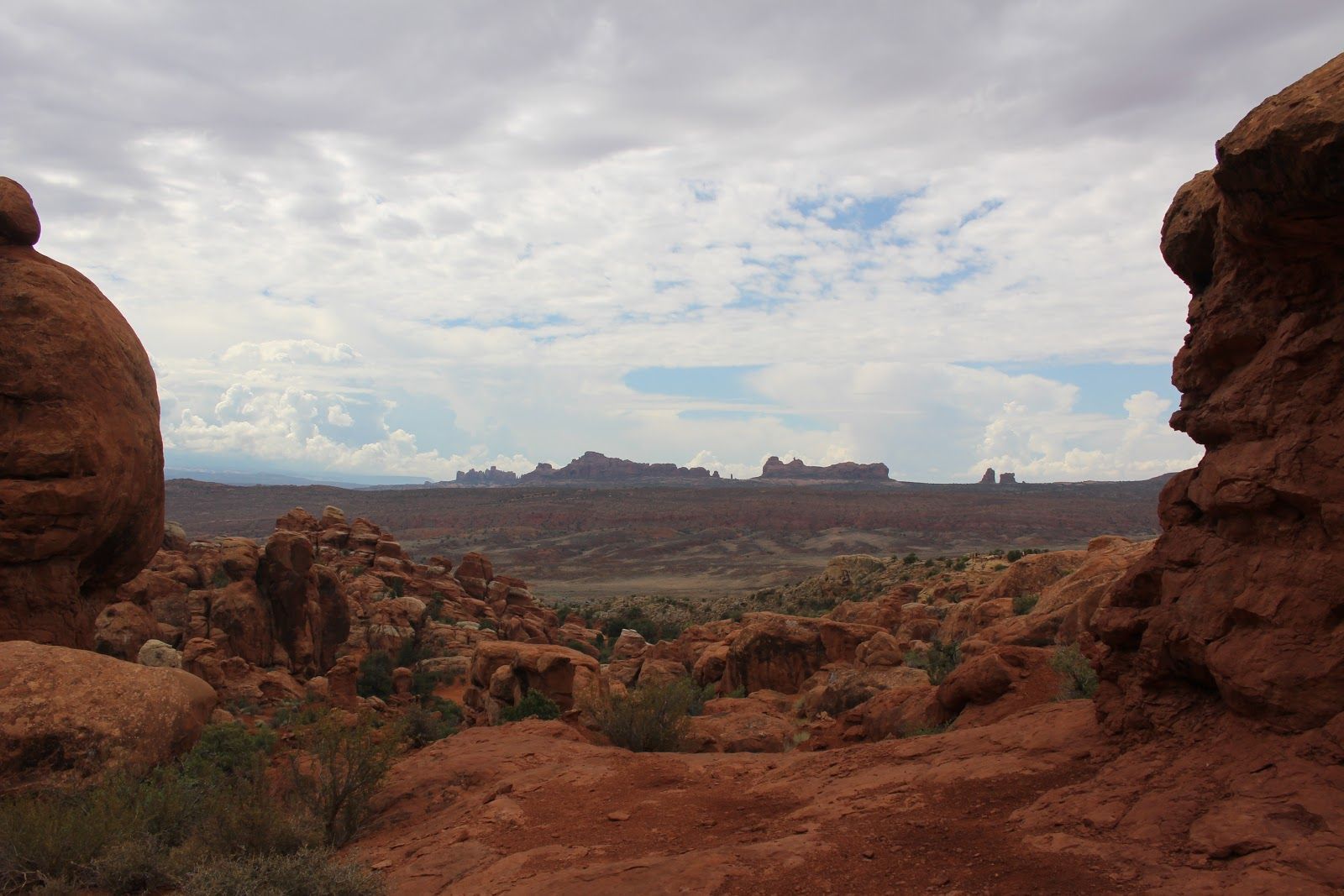 Red rock desert landscape with distant mesas under a cloudy sky