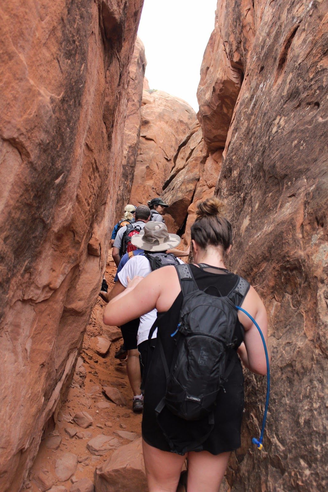 Hikers in a narrow red rock canyon, climbing a rocky trail between tall cliffs