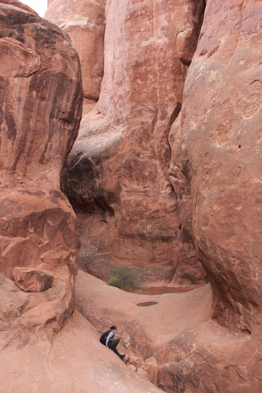 Person sitting in a narrow red rock canyon with towering sandstone walls