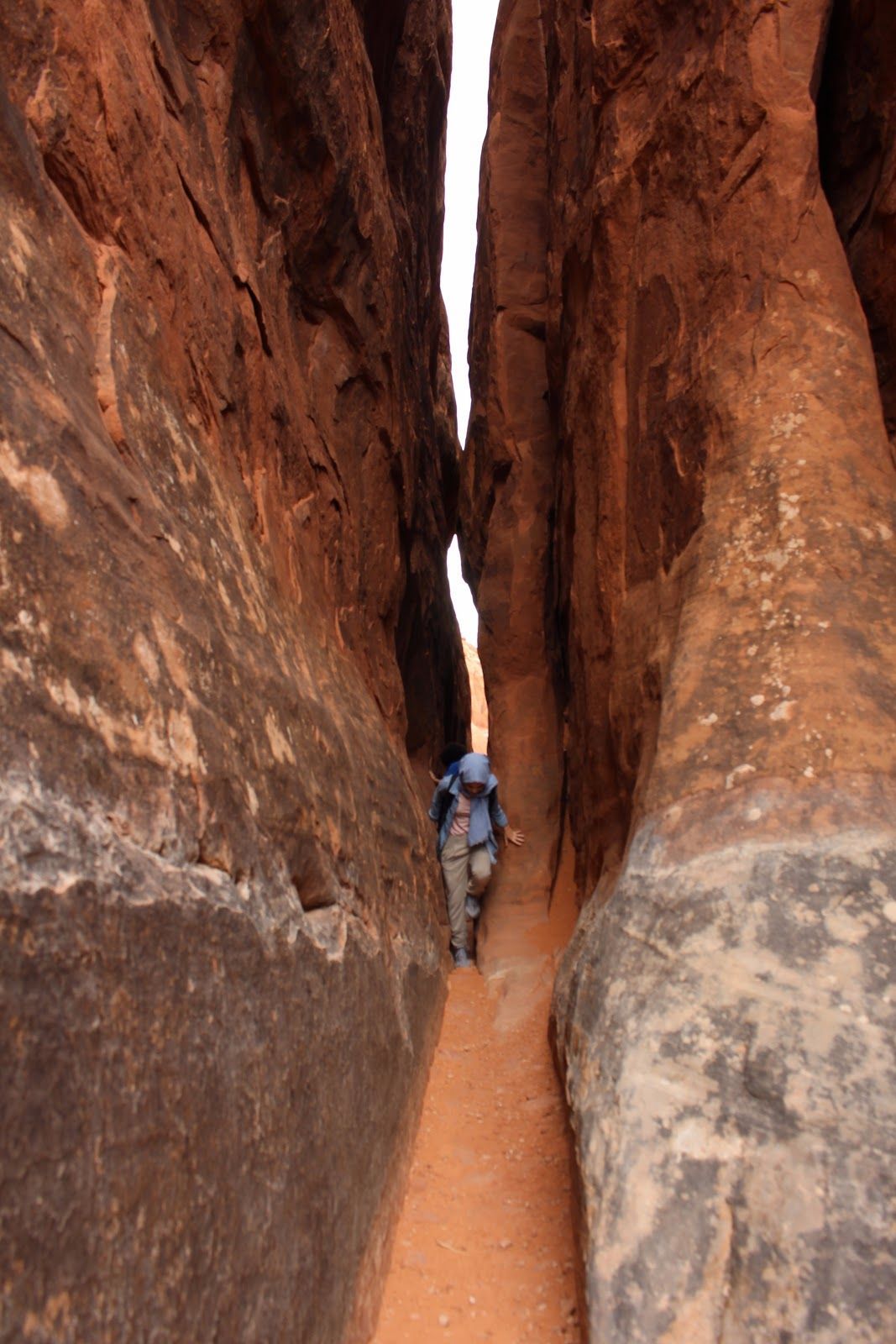 Person hiking between tall red sandstone canyon walls.