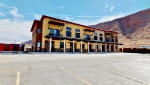 Yellow two-story lodge with blue windows in a mountain desert, seen across an empty paved lot