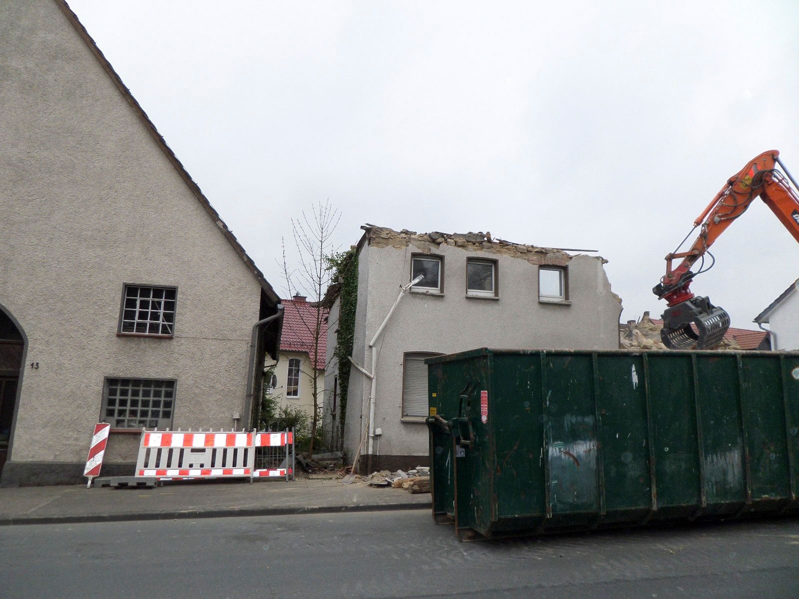 Ein Haus wird abgerissen, davor steht ein grüner Müllcontainer