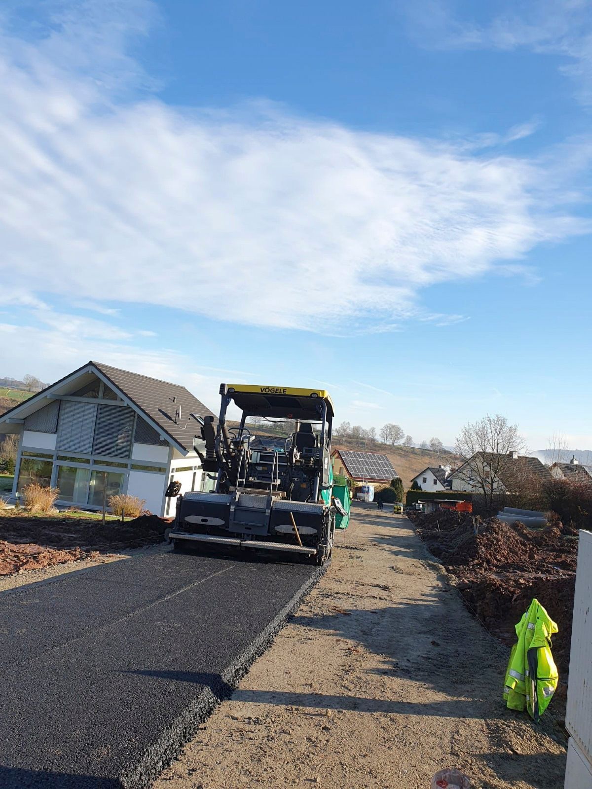 Eine Maschine asphaltiert eine Straße vor einem Haus.